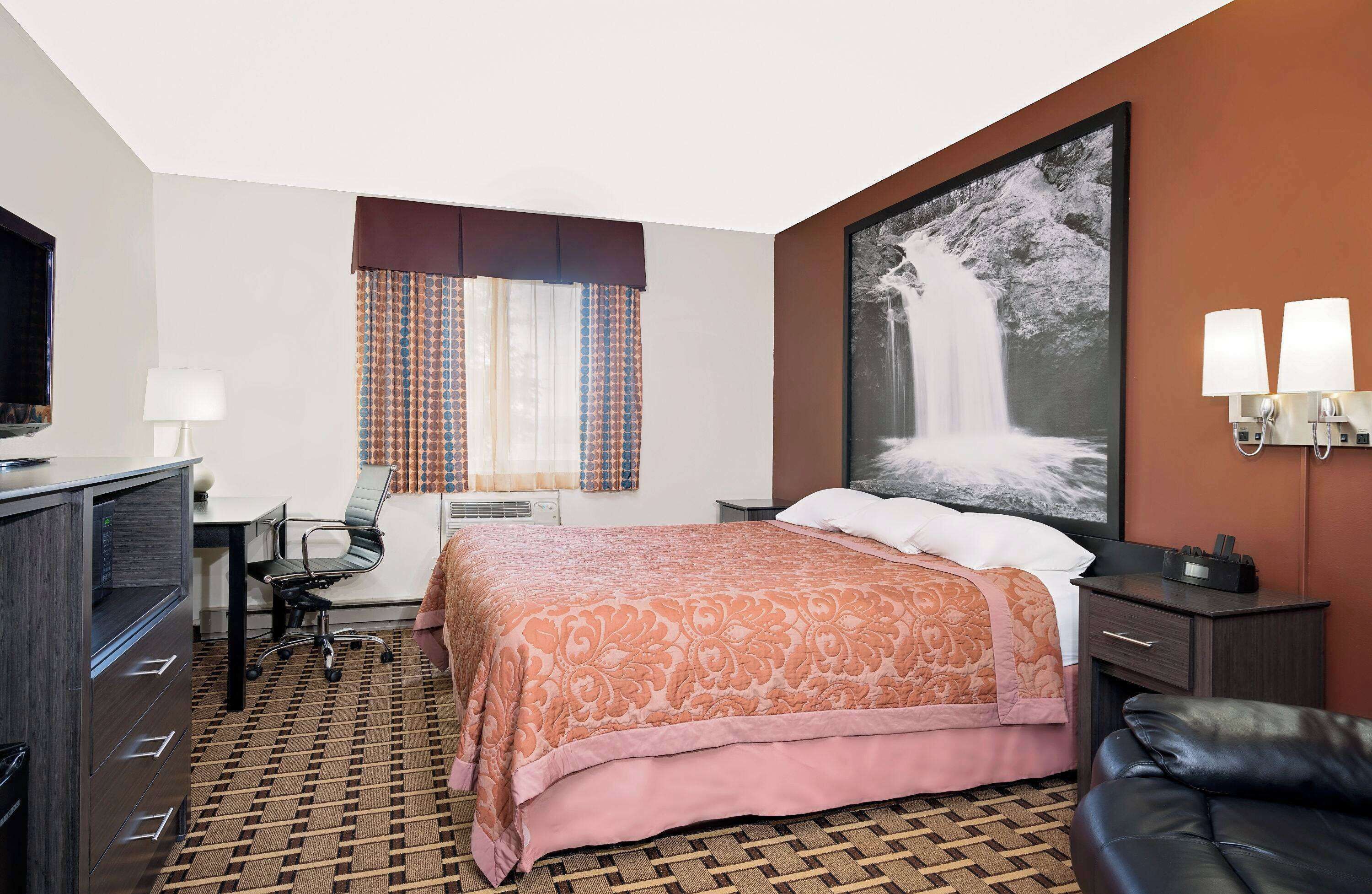 Ein Hotelzimmer mit Bett, Schreibtisch, Stuhl und einem großen Fenster mit Vorhängen.