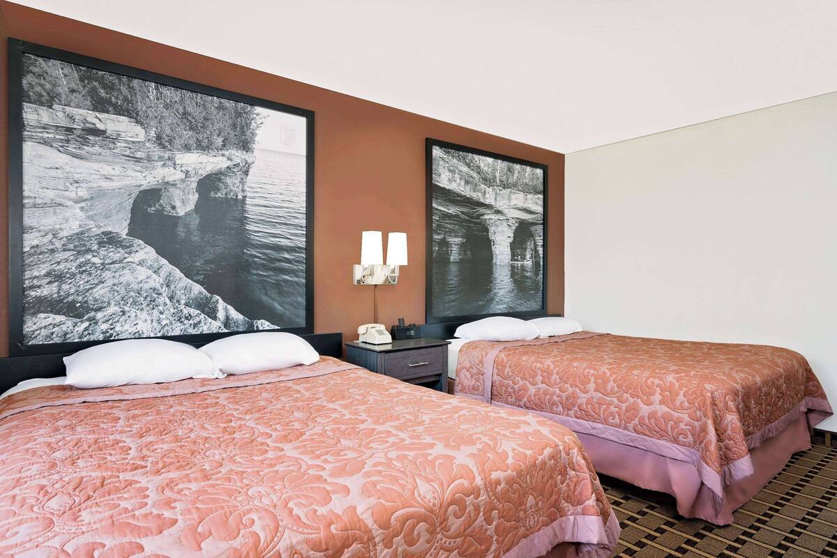 Une chambre d’hôtel avec deux lits, une table de chevet, un téléphone et deux lampes fixées au mur.