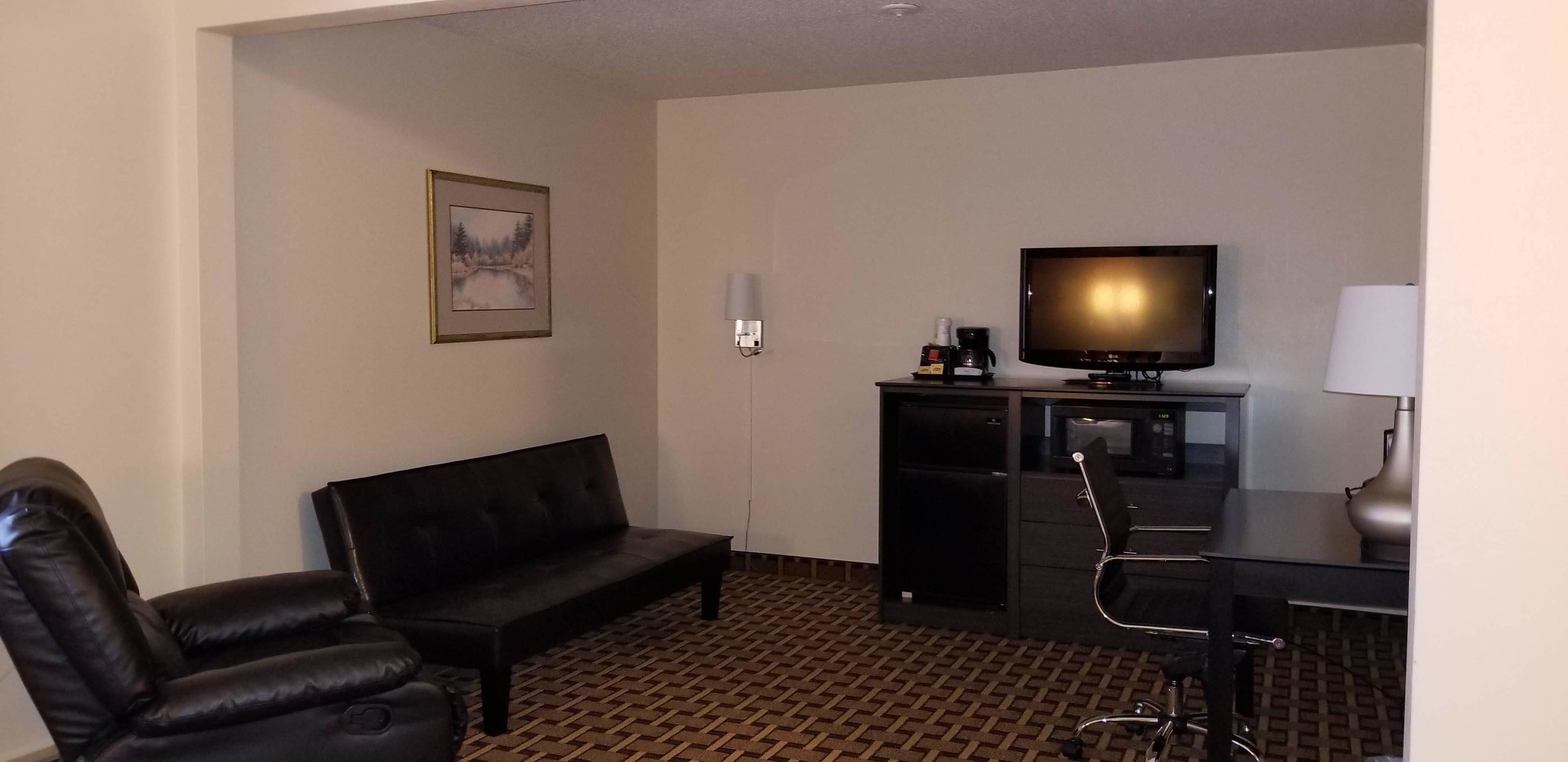 A hotel room with a black leather sofa, a desk with a chair, a television, a coffee maker, and a framed picture on the wall.