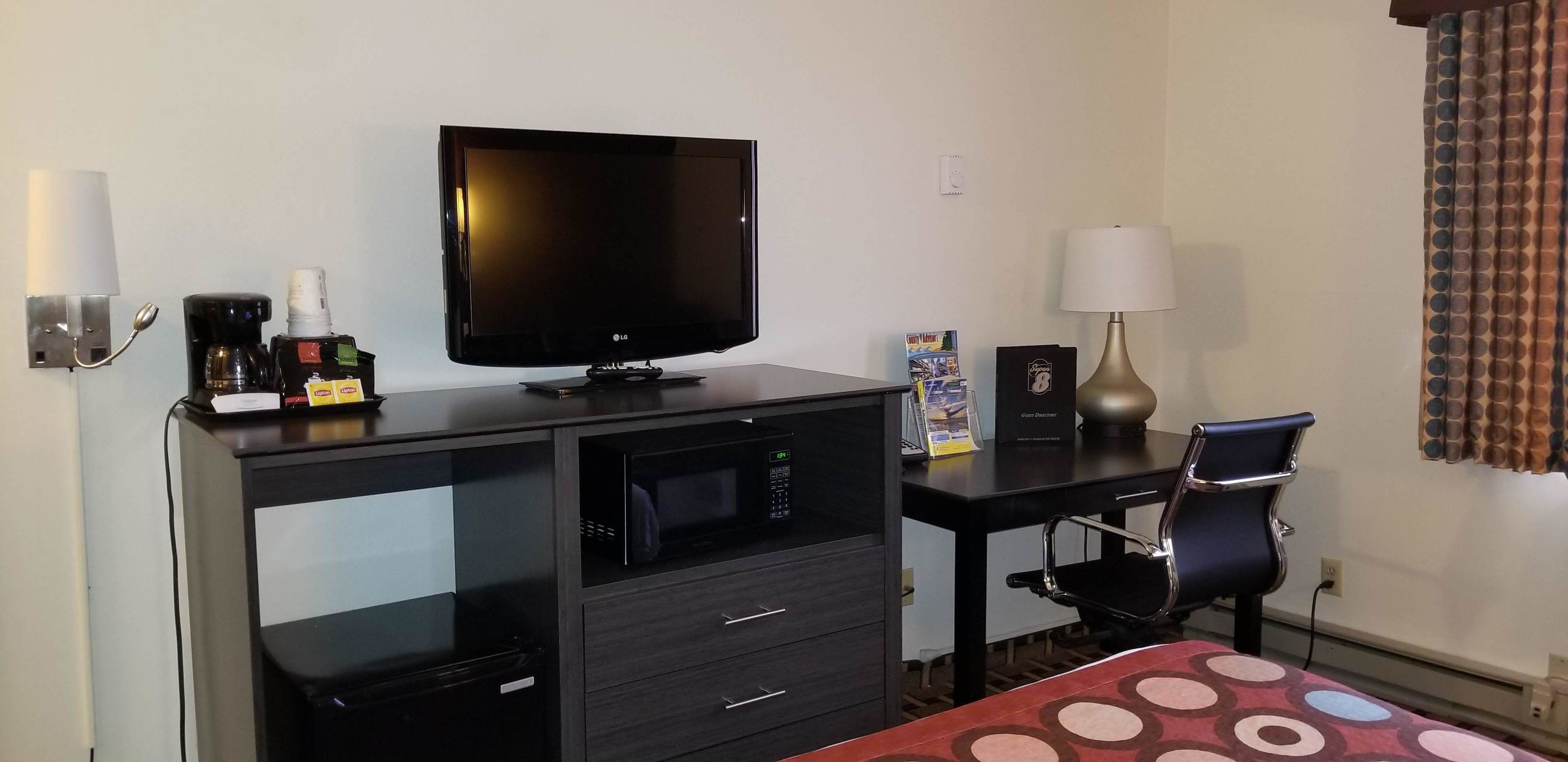 Habitación de hotel con escritorio, televisor, microondas, cafetera, lámpara, silla y cama con colcha de lunares.