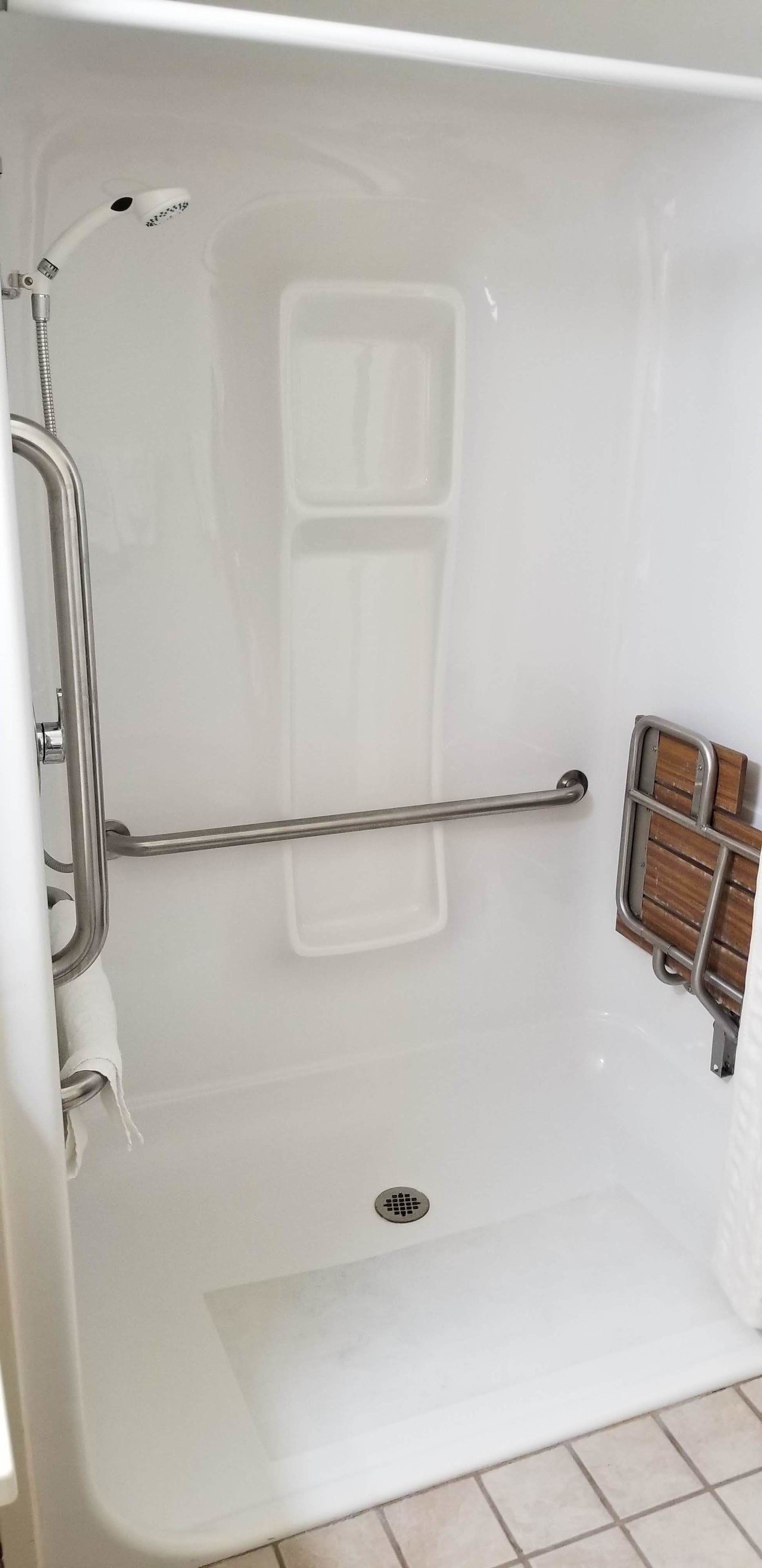 A white bathtub with a showerhead, grab bars, and a wooden panel.