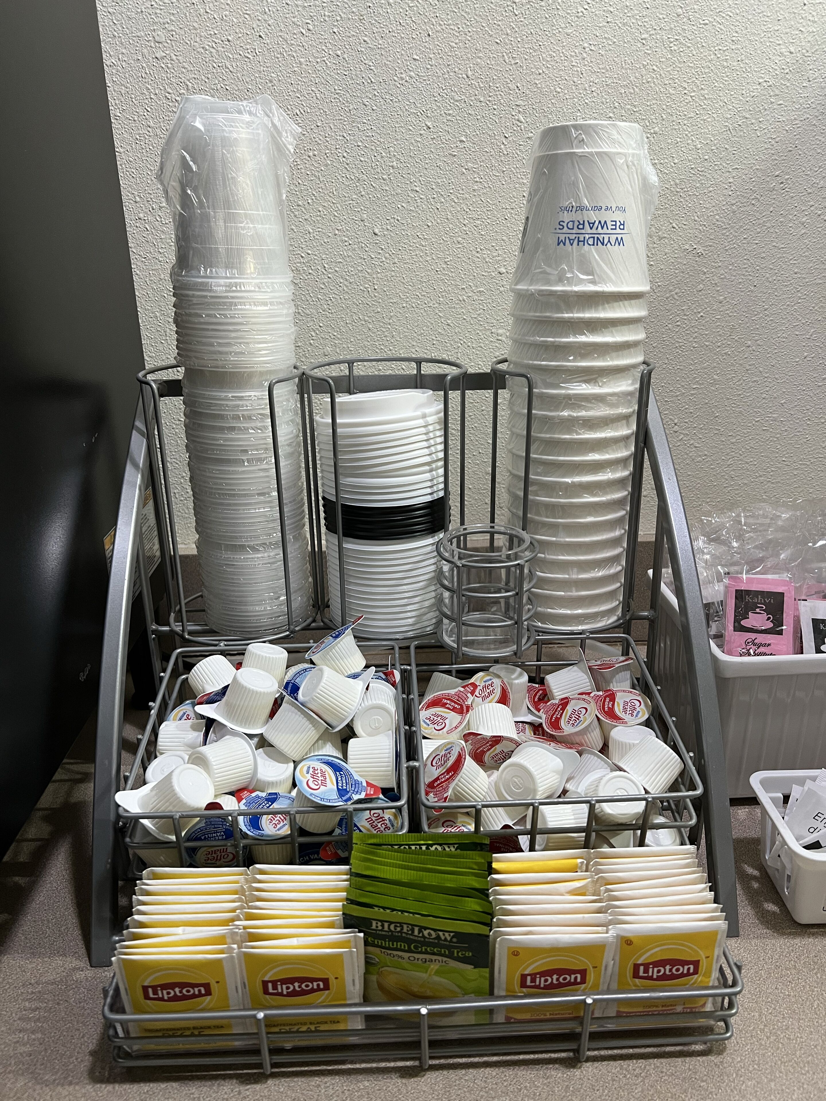A display of disposable cups, plates, and Lipton tea packets in a metal rack.