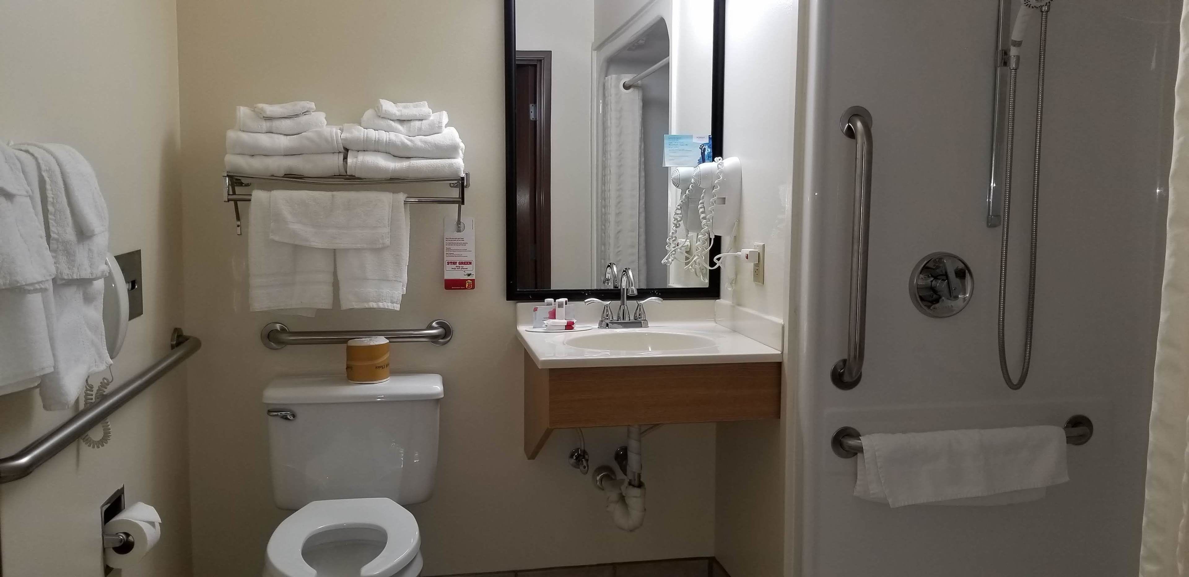 A bathroom with a toilet, sink, and shower. There are towels stacked on a rack and a hand dryer.