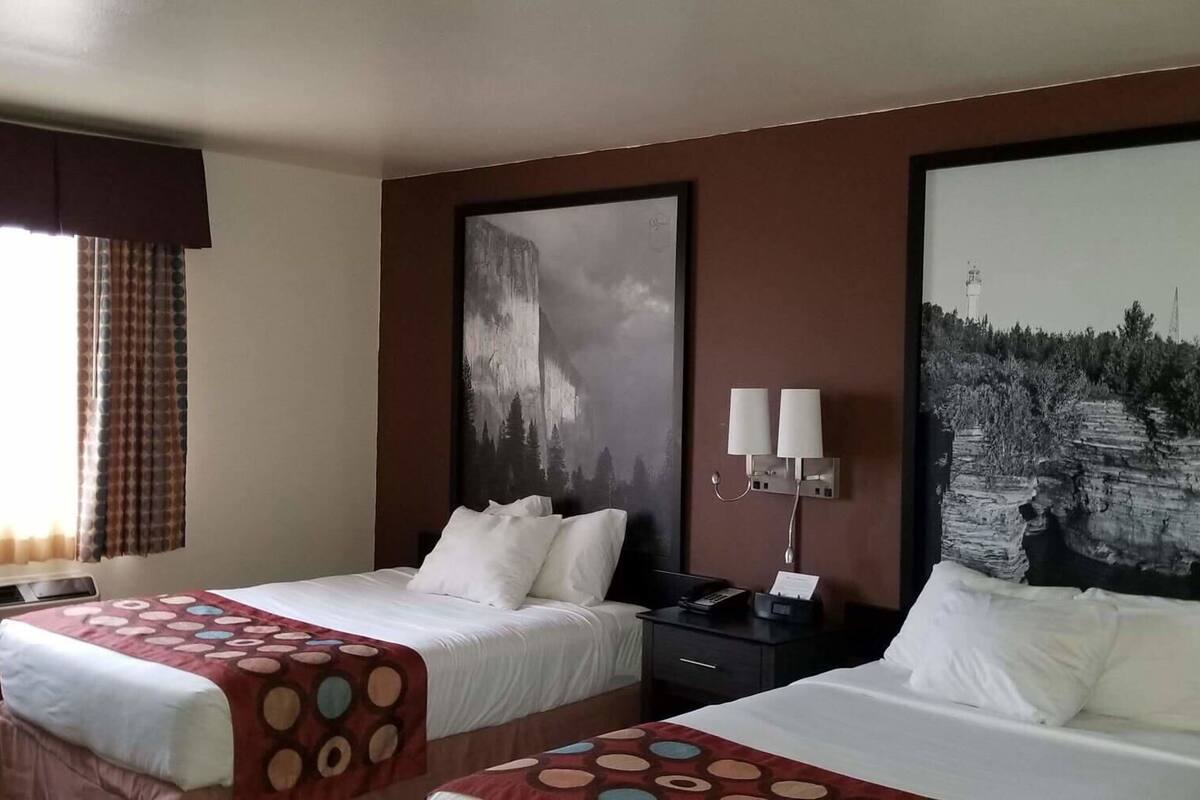 Une chambre d’hôtel avec deux lits, une grande fenêtre avec des rideaux, un tableau au mur et une table de chevet avec une lampe.