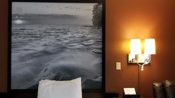 Ein gerahmtes Foto von stürmischer See an einer Wand, eine Nachttischlampe und ein Kissen auf einem Bett.