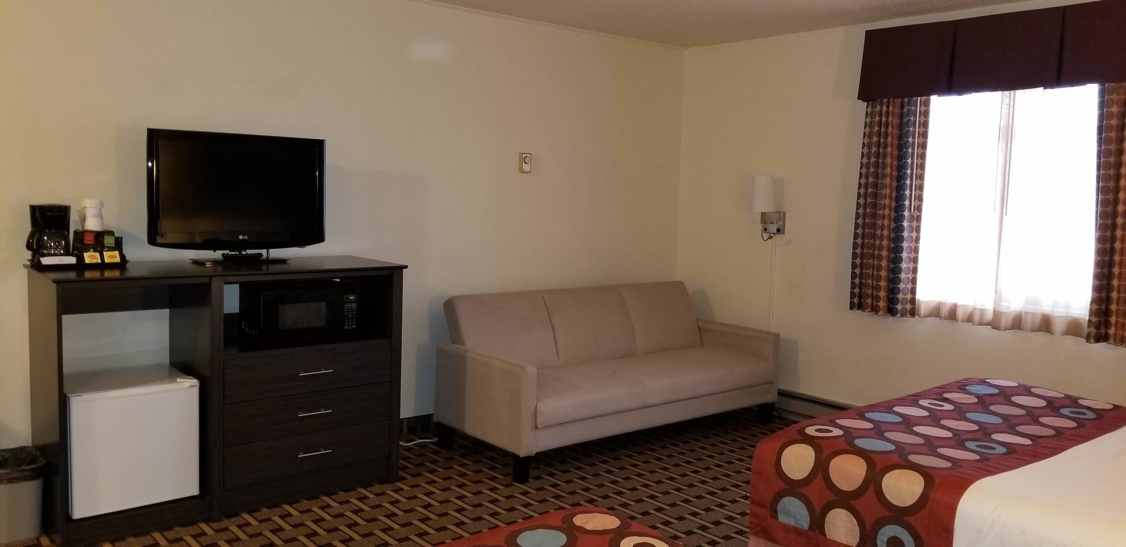 A hotel room with a television, a sofa, a bed with a patterned bedspread, a small refrigerator, and a patterned floor.