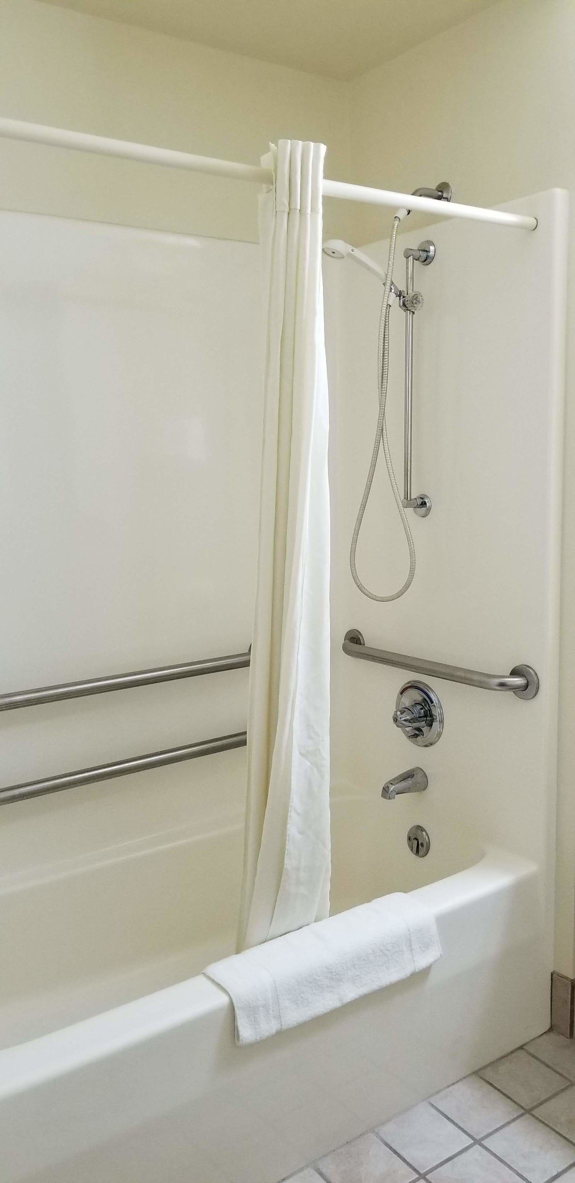 A bathroom with a white bathtub, a shower with a handheld showerhead, and a grab bar.