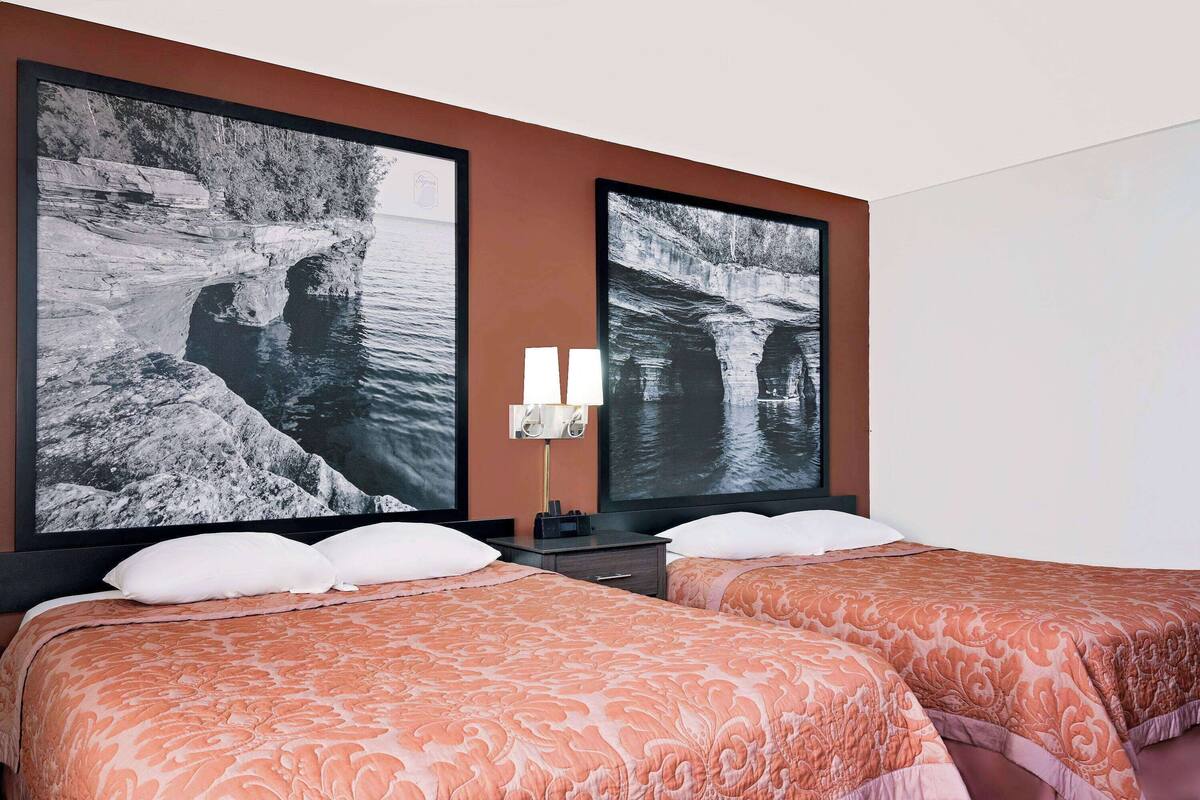 Une chambre d’hôtel avec deux lits, chacun recouvert d’une couvre-lit à motifs, une table de chevet avec une lampe, et deux grandes photographies en noir et blanc accrochées au mur.