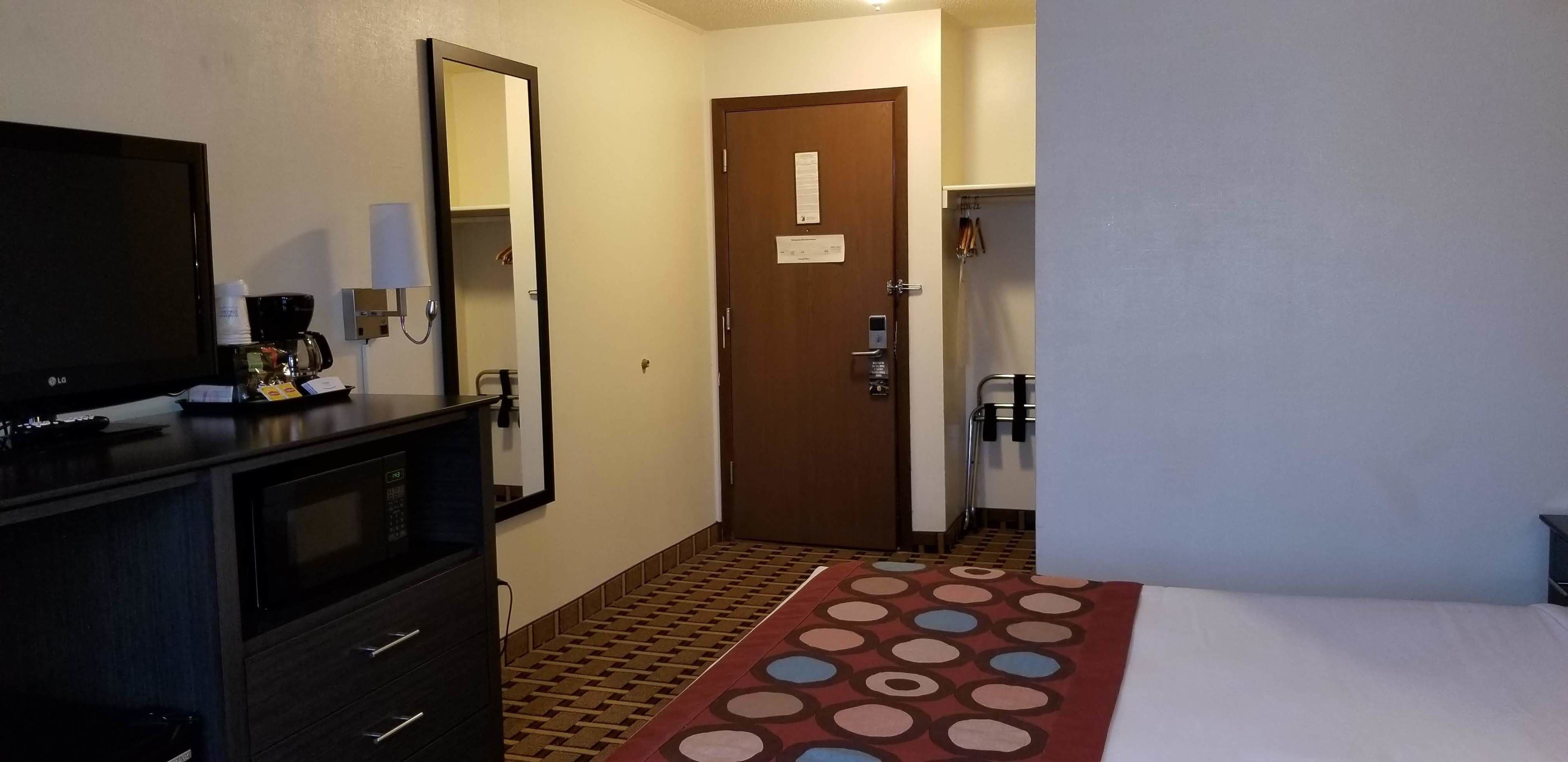 Habitación de hotel con cama, televisión, cómoda, espejo, puerta y alfombra estampada.