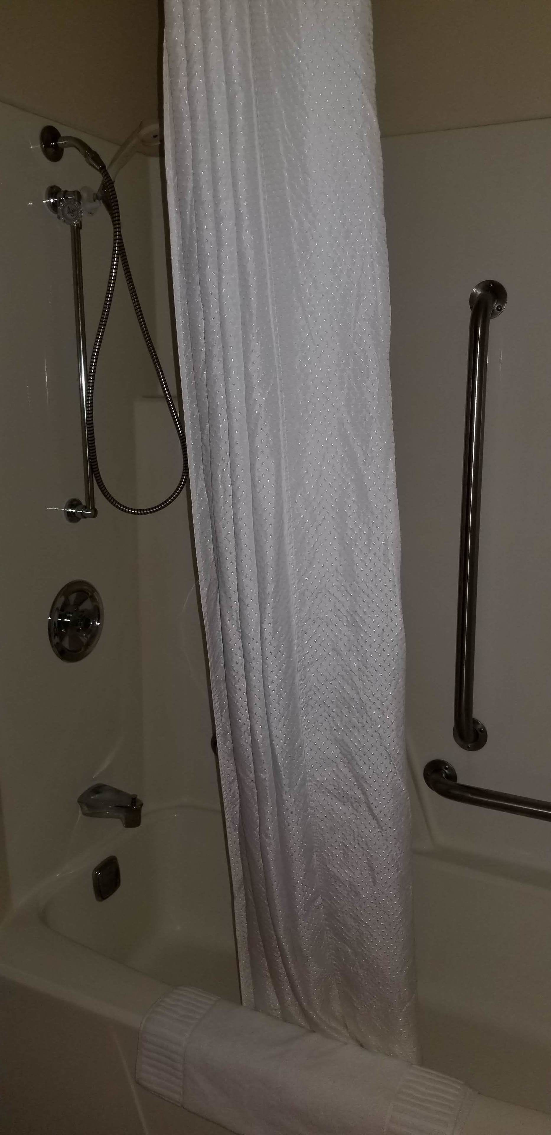A shower area with a handheld showerhead, a glass-enclosed tub, and a grab bar.