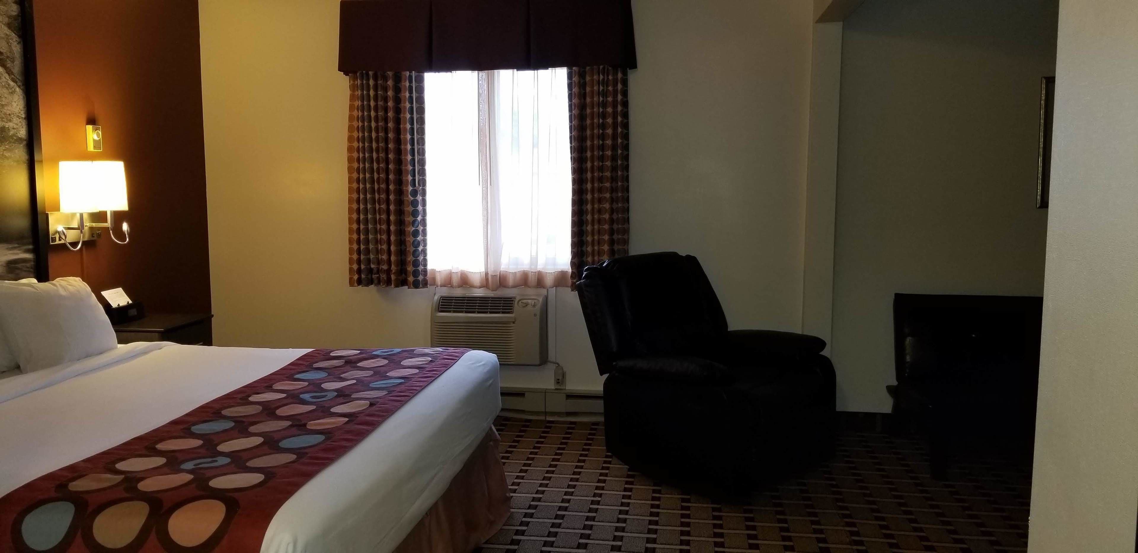 A hotel room with a bed, a chair, a desk, a lamp, and a window with curtains.