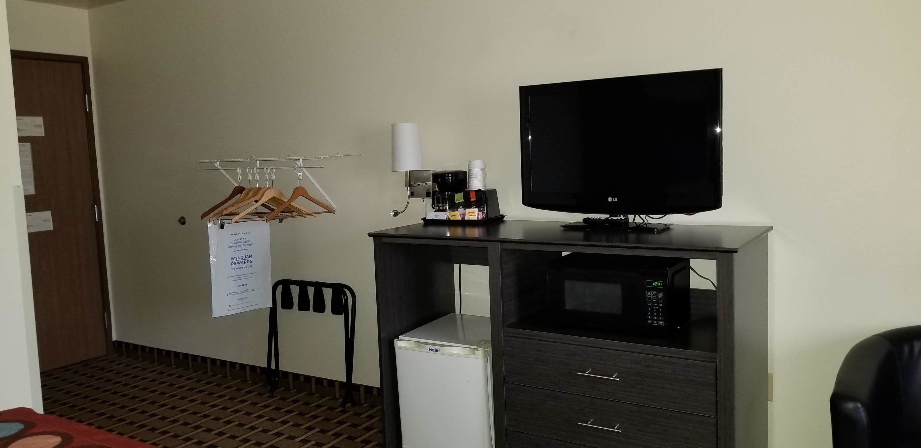 A hotel room with a desk, a television, a coffee maker, a mini fridge, a chair, and a clothes drying rack.