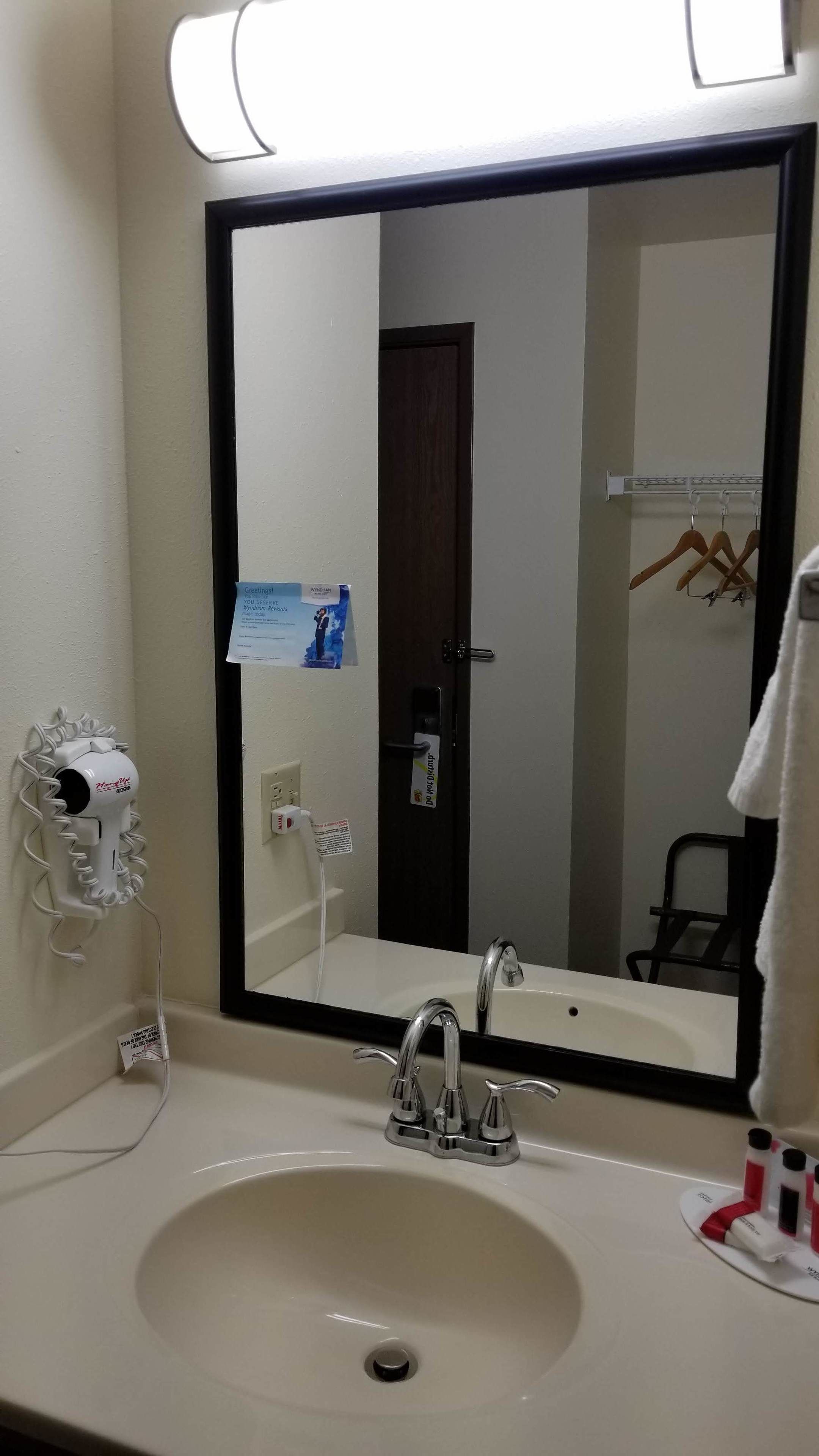 A hotel bathroom with a large mirror, a sink with a modern faucet, a hairdryer, and a towel rack.
