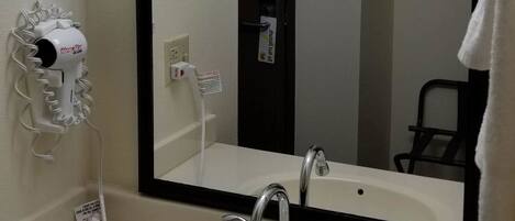 A hotel bathroom with a large mirror, a sink with a modern faucet, a hairdryer, and a towel rack.