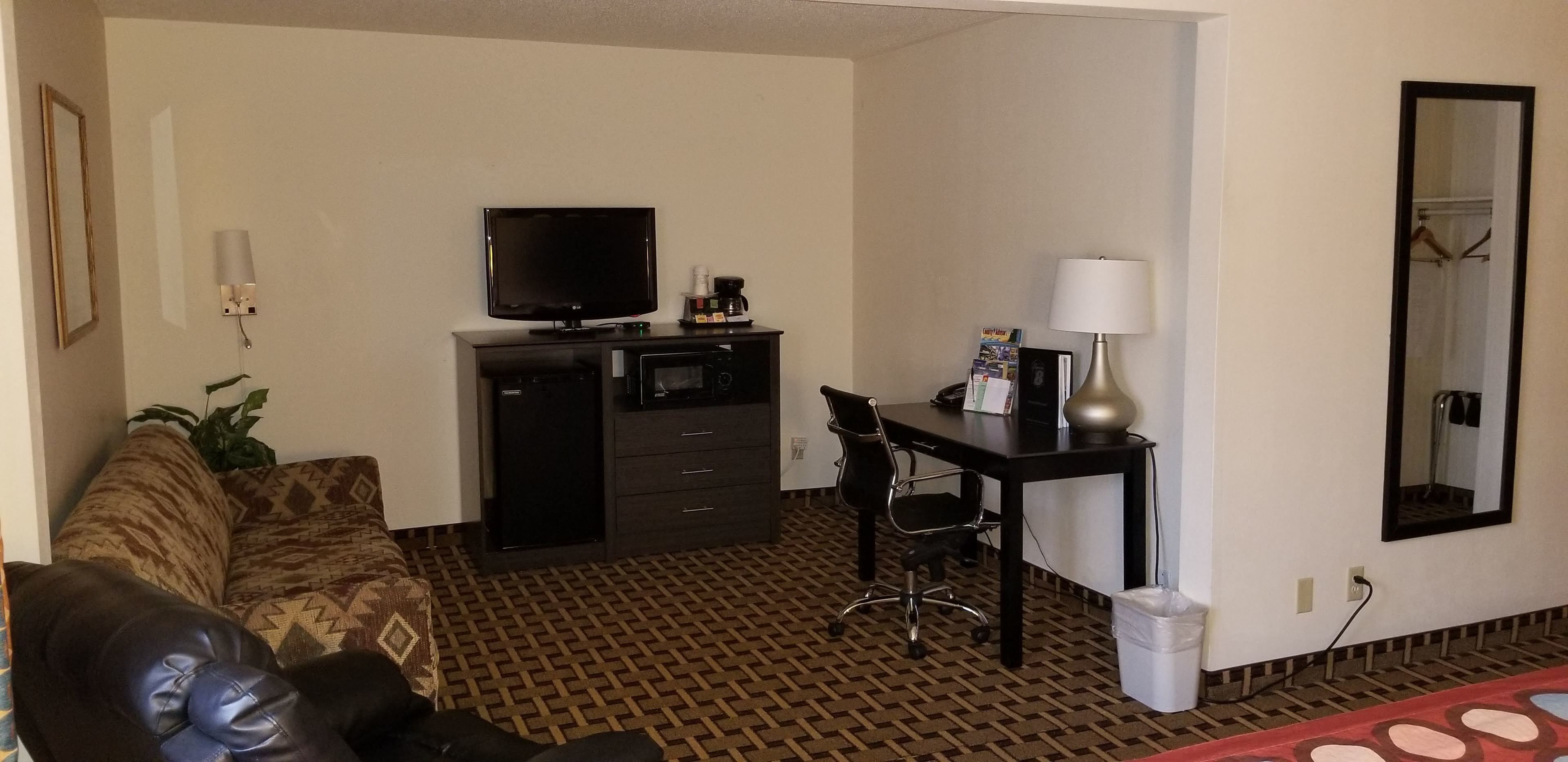 Ein Hotelzimmer mit einer Couch, einem Schreibtisch mit Stuhl, einem Fernseher, einer Kaffeemaschine und einem Papierkorb.
