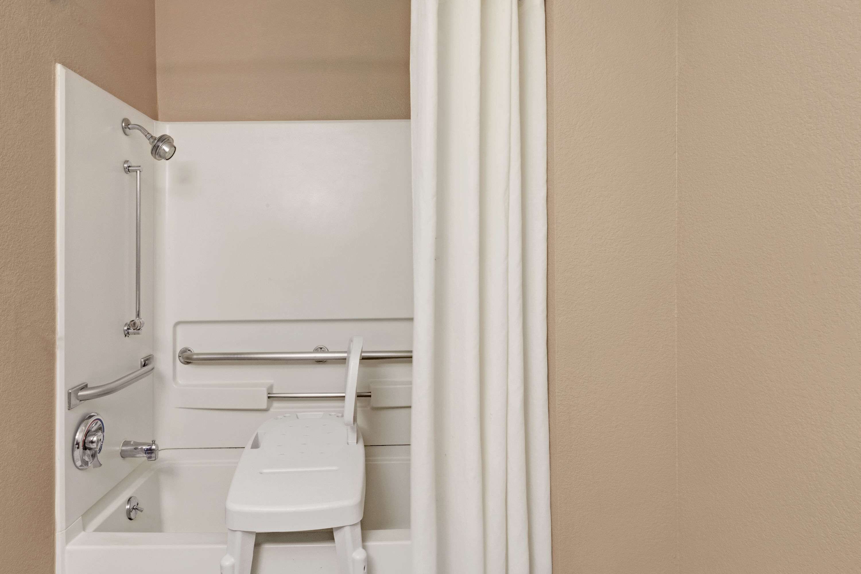 A white bathroom with a shower, grab bars, and a toilet.