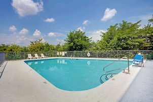 A swimming pool with a metal ladder, surrounded by a metal fence. There are lounge chairs along the poolside.