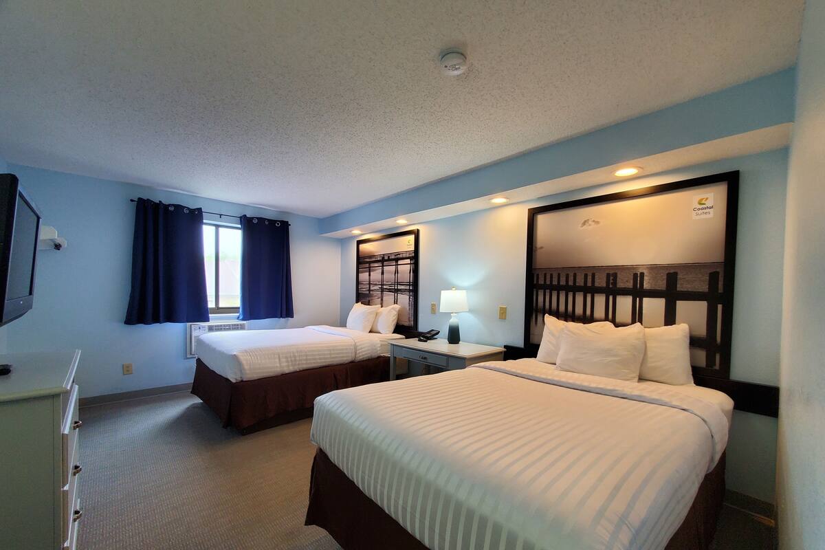 Ein Hotelzimmer mit zwei Betten, einem Schreibtisch, einer Lampe und einem Fernseher.