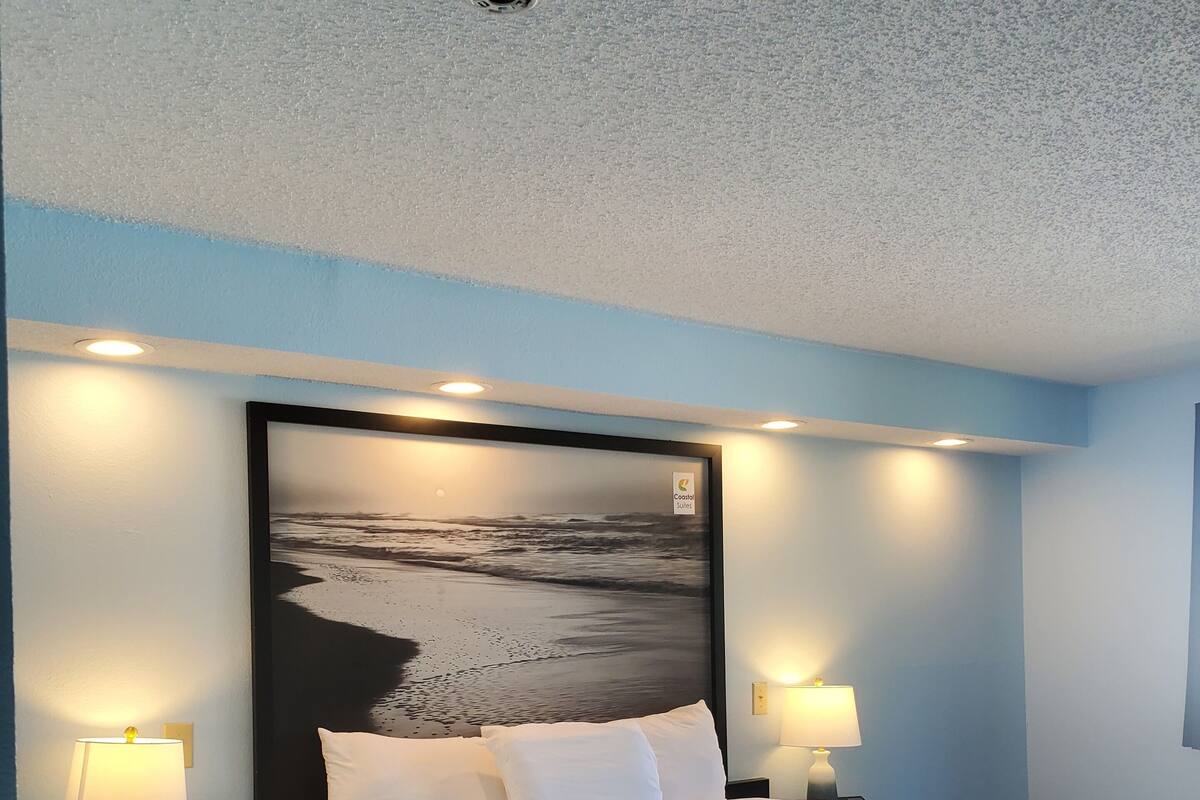 Ein Hotelzimmer mit einem großen Bett, zwei Nachttischen mit Lampen, einem kleinen Tisch und einem Wandbild.