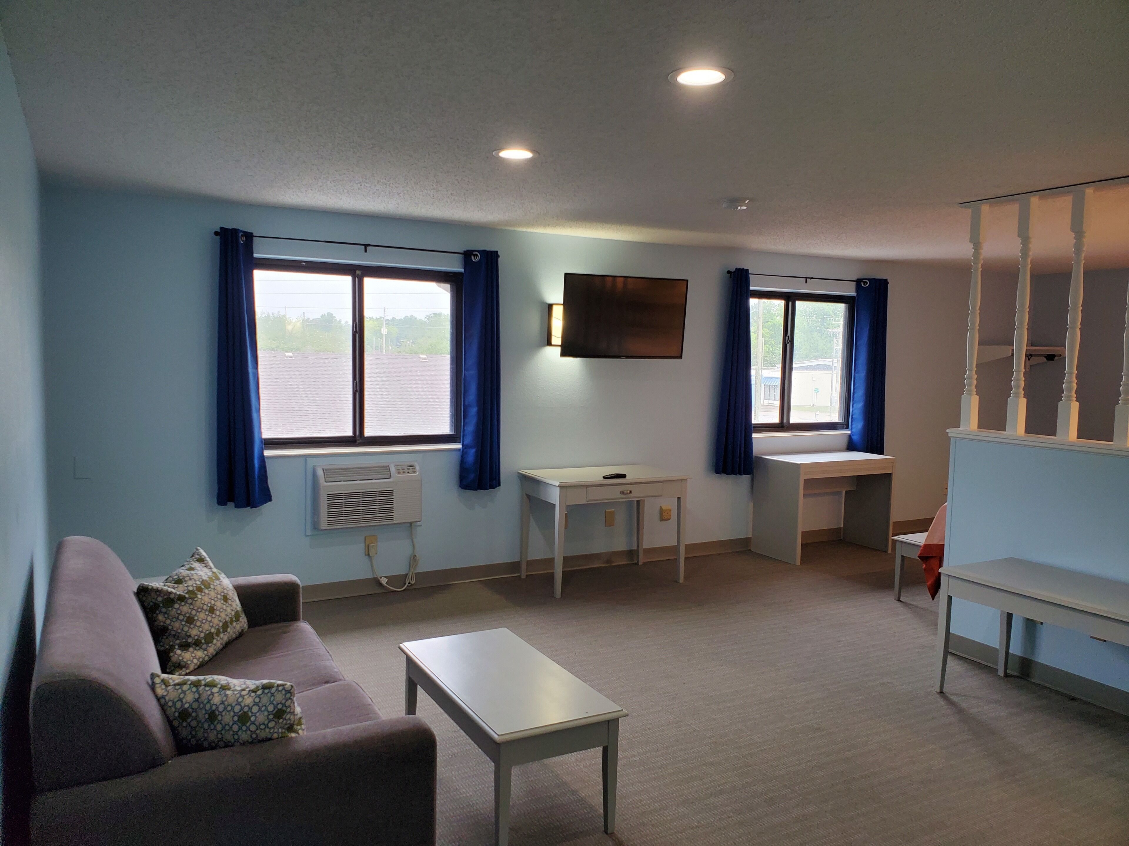 Une pièce comprenant un canapé, une petite table, un bureau et un téléviseur fixé au mur.