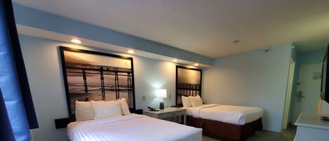 A hotel room with two beds, a desk, a mirror, and a small refrigerator.