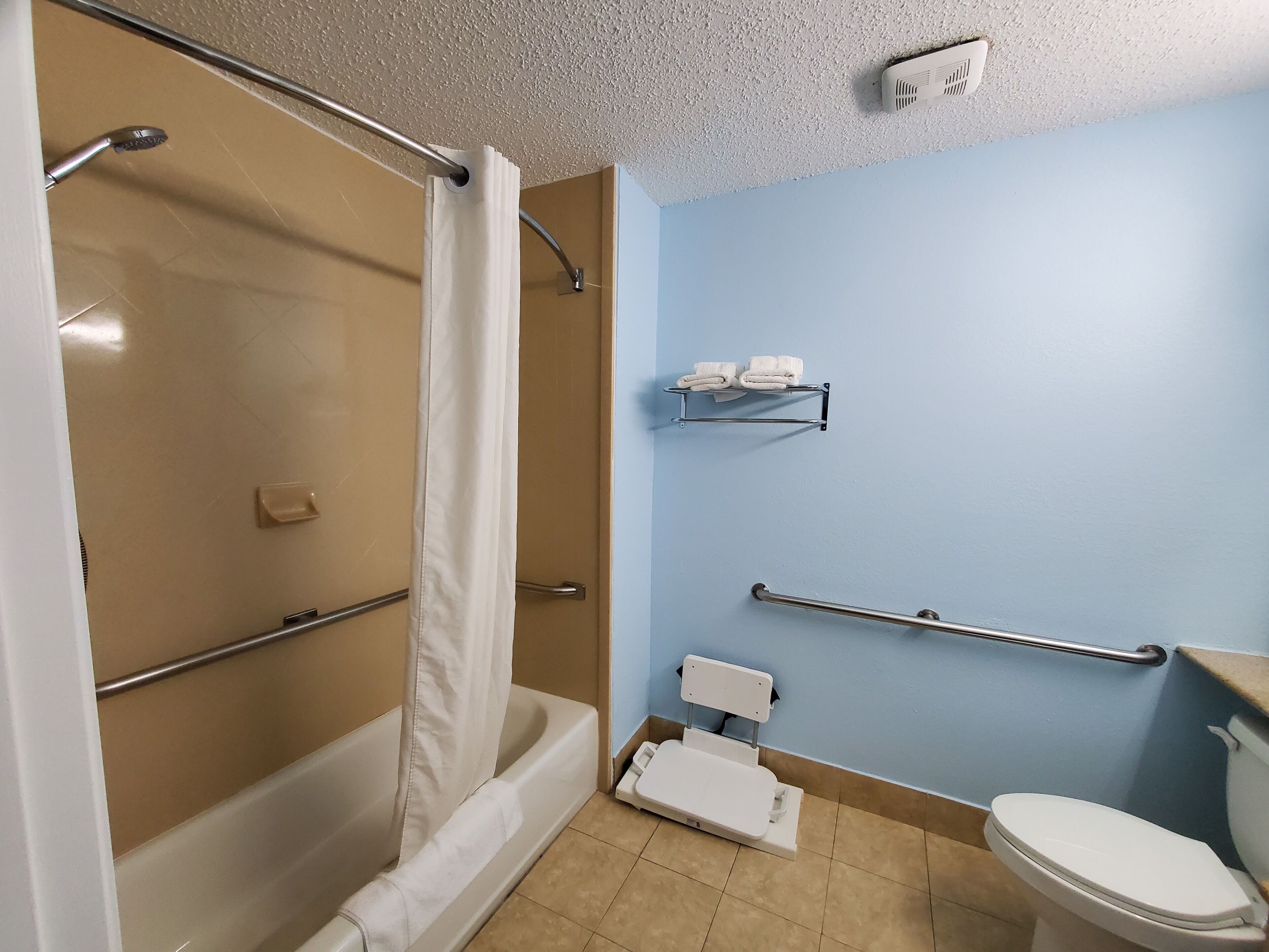 Une salle de bain équipée d’une douche, de toilettes, de barres d’appui, d’un porte-serviettes et d’une lunette de toilette surélevée.