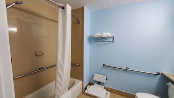 Une salle de bain équipée d’une douche, de toilettes, de barres d’appui, d’un porte-serviettes et d’une lunette de toilette surélevée.