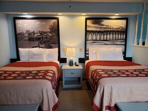 Ein Hotelzimmer mit zwei Betten, jeweils mit einem gemusterten Überwurf, einem Nachttisch mit Lampe und einer kleinen Schublade.
