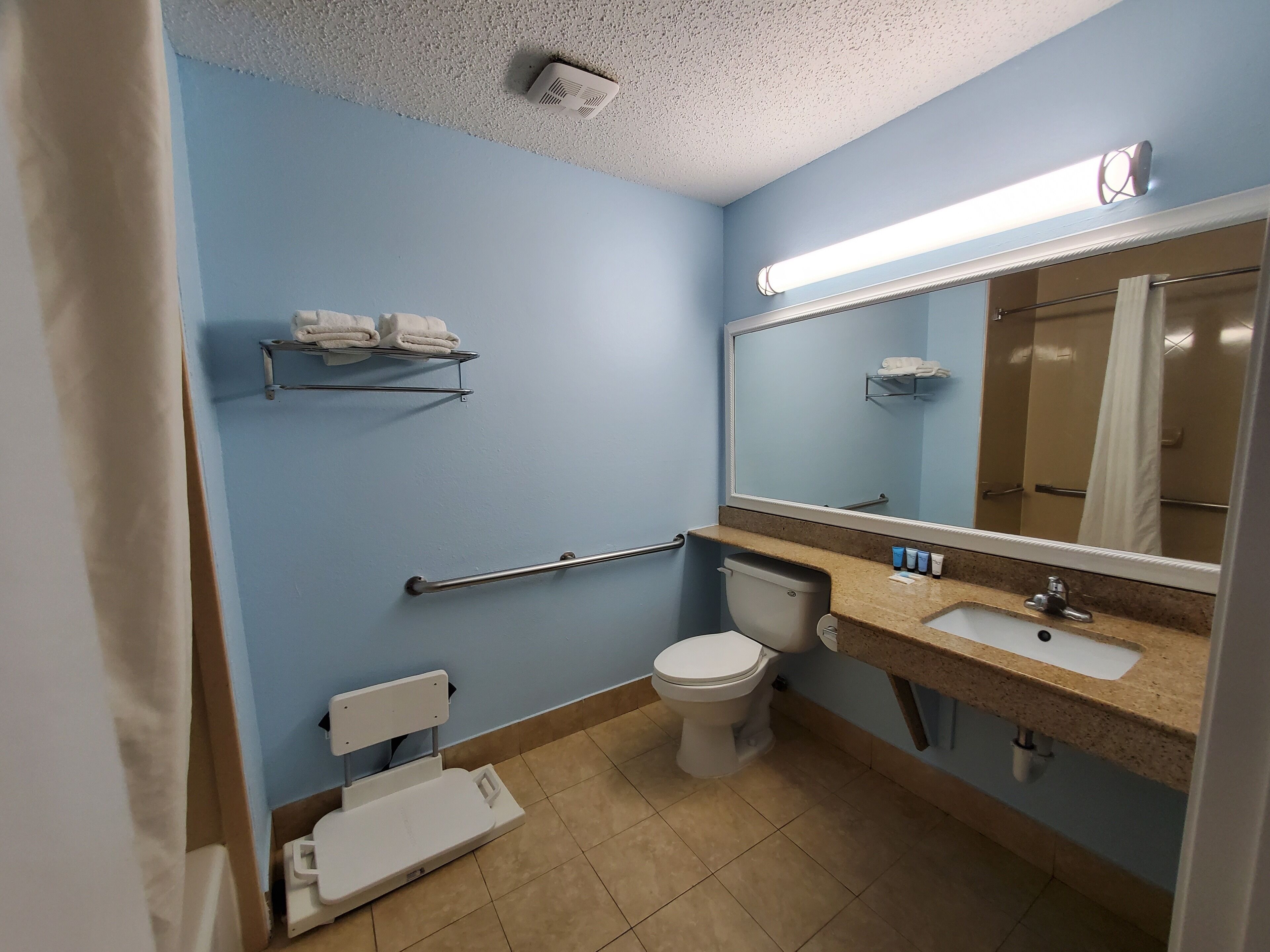 A bathroom with a toilet, sink, mirror, towel rack, and a grab bar.