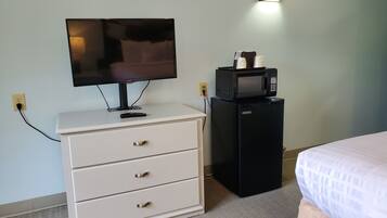 A hotel room with a white dresser, a black minibar, a television, and a bed with a white bedspread.