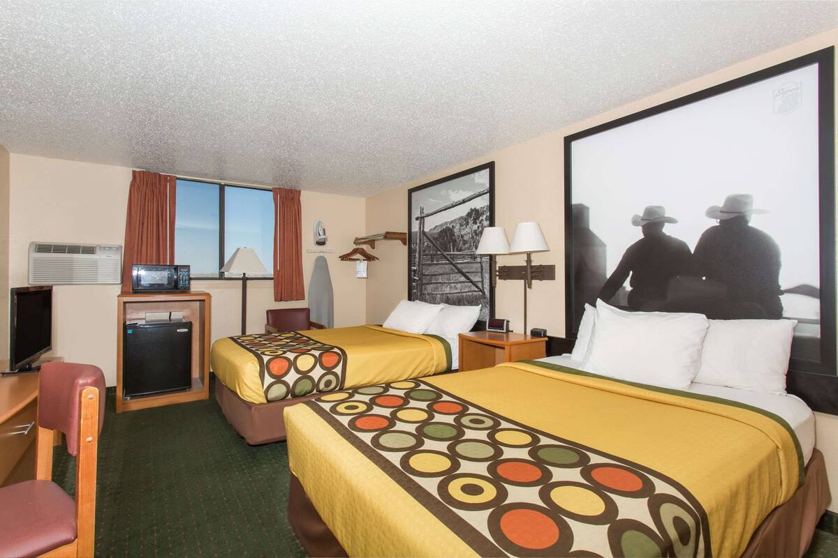 A hotel room with two beds, a desk, a TV, a mini-fridge, and a large poster on the wall.