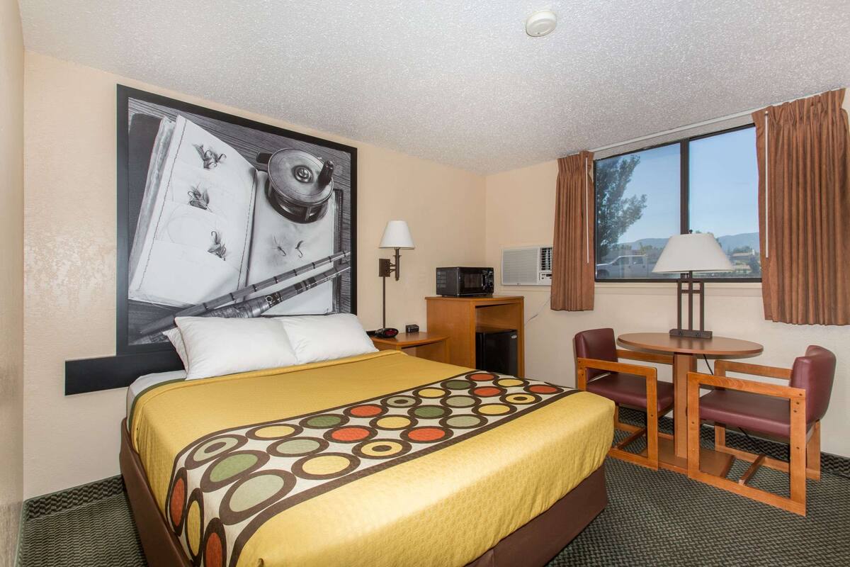 A hotel room with a bed, a desk with a chair, a television, and a window with curtains.