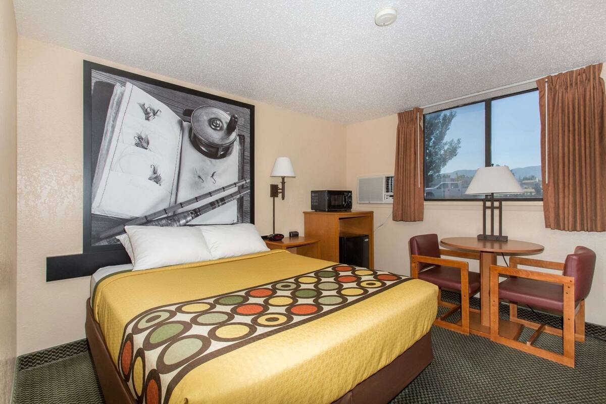A hotel room with a bed, a desk with a computer, a chair, a lamp, and a window with curtains.