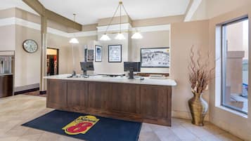 Un hall d’hôtel avec un comptoir d’accueil, une horloge, des tableaux encadrés, un grand vase et une fenêtre.