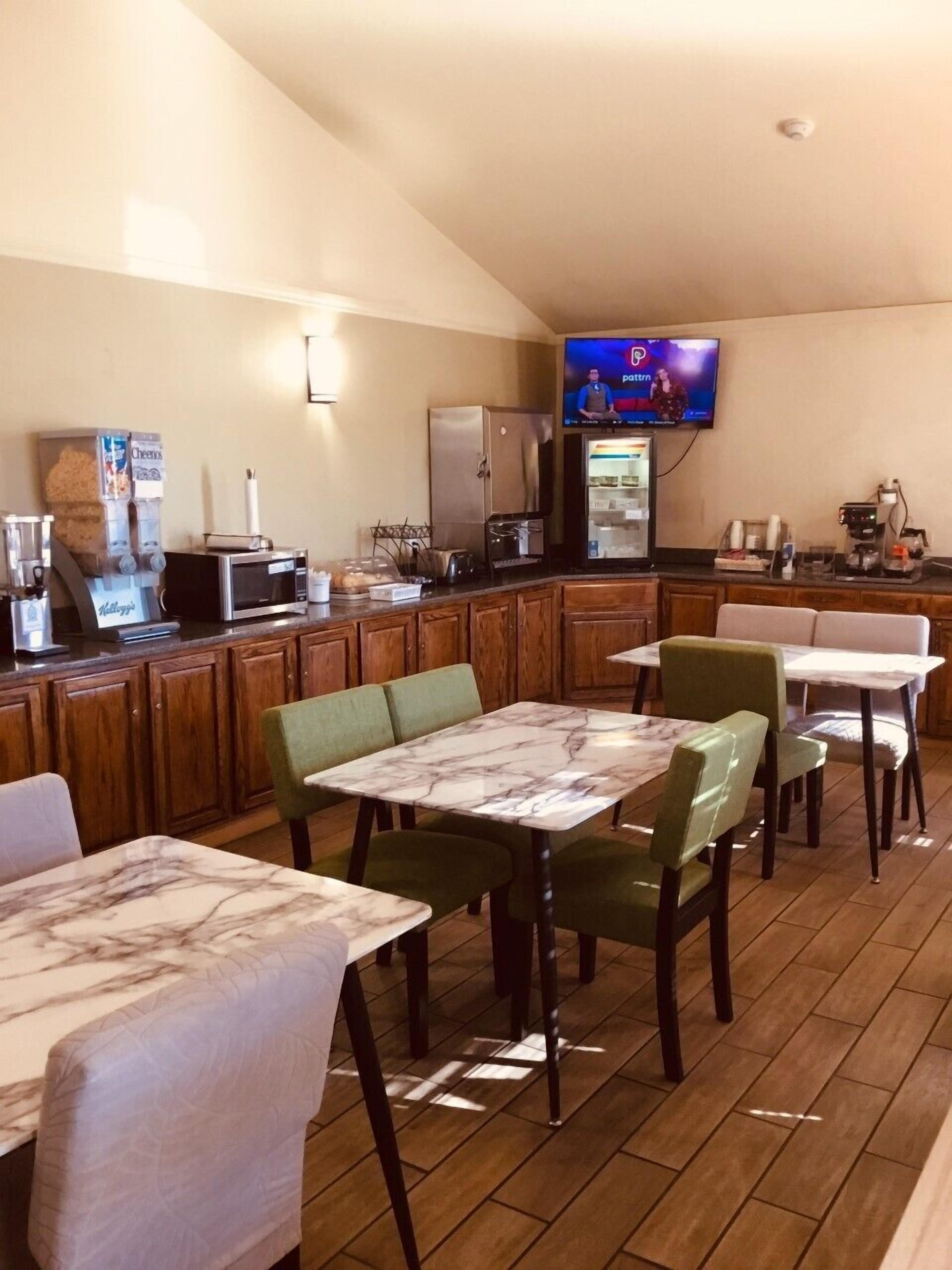 A restaurant with marble-topped tables and green chairs, a television mounted on the wall, and a refrigerator in the background.