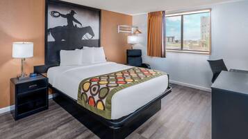 Hotelkamer met een groot bed, een bureau, een stoel, een nachtkastje met lamp en een raam met gordijnen.