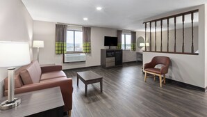 Een moderne woonkamer met een bank, salontafel en fauteuil. Er is een televisie, een kitchenette en een trap.