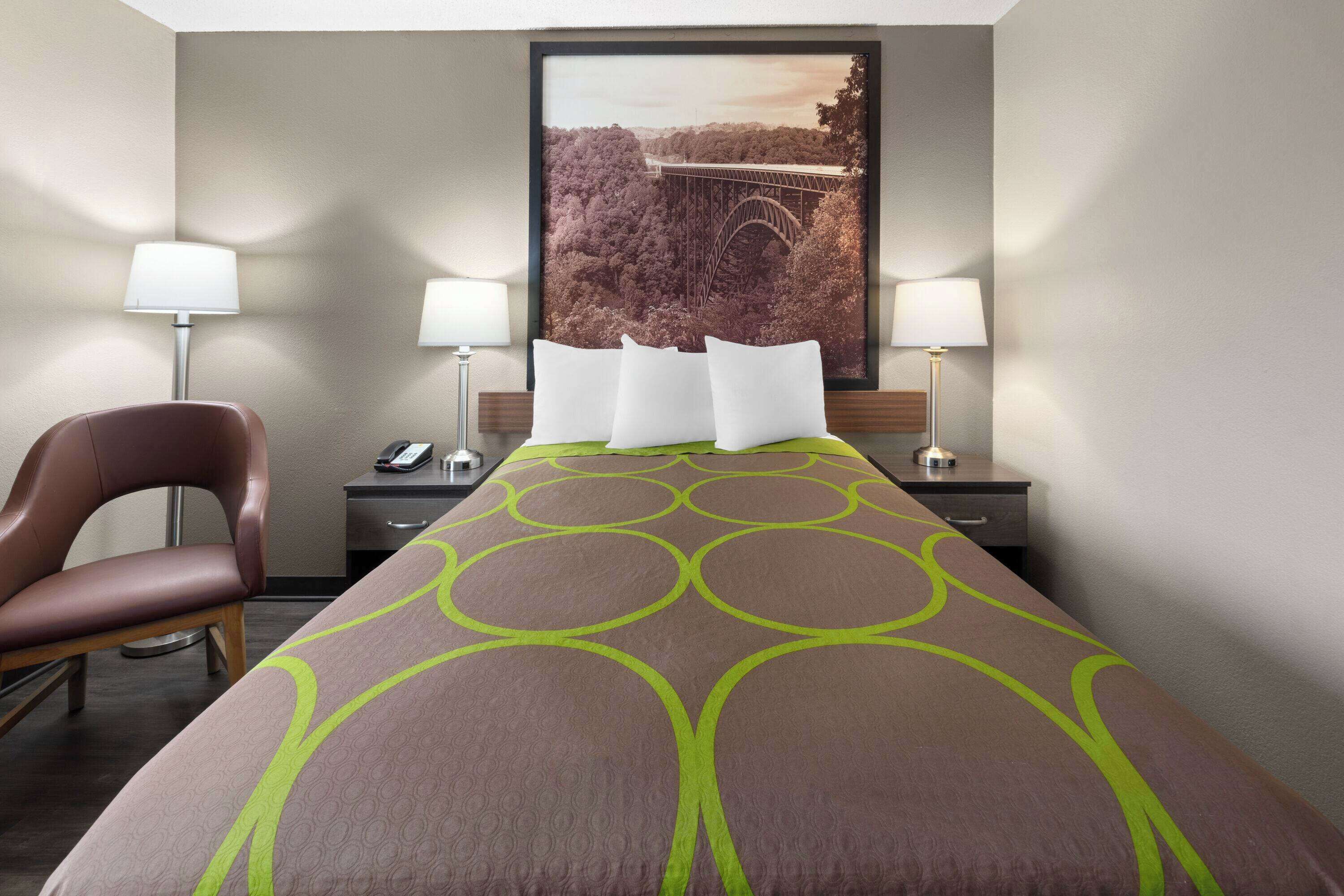 A hotel room with a bed, two bedside lamps, a chair, a desk, and a framed picture on the wall.
