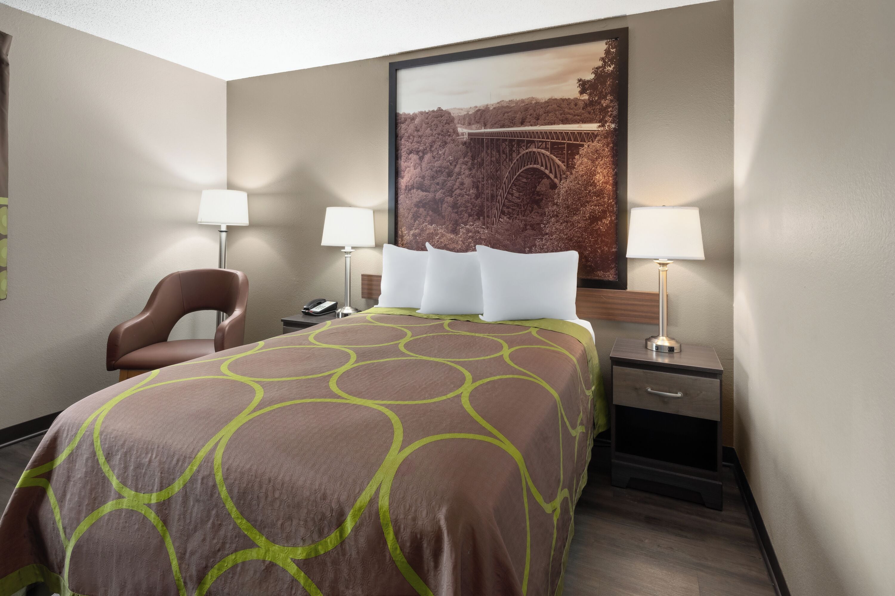 Habitación de hotel con una cama grande, dos mesitas de noche con lámparas, una silla y un cuadro en la pared.