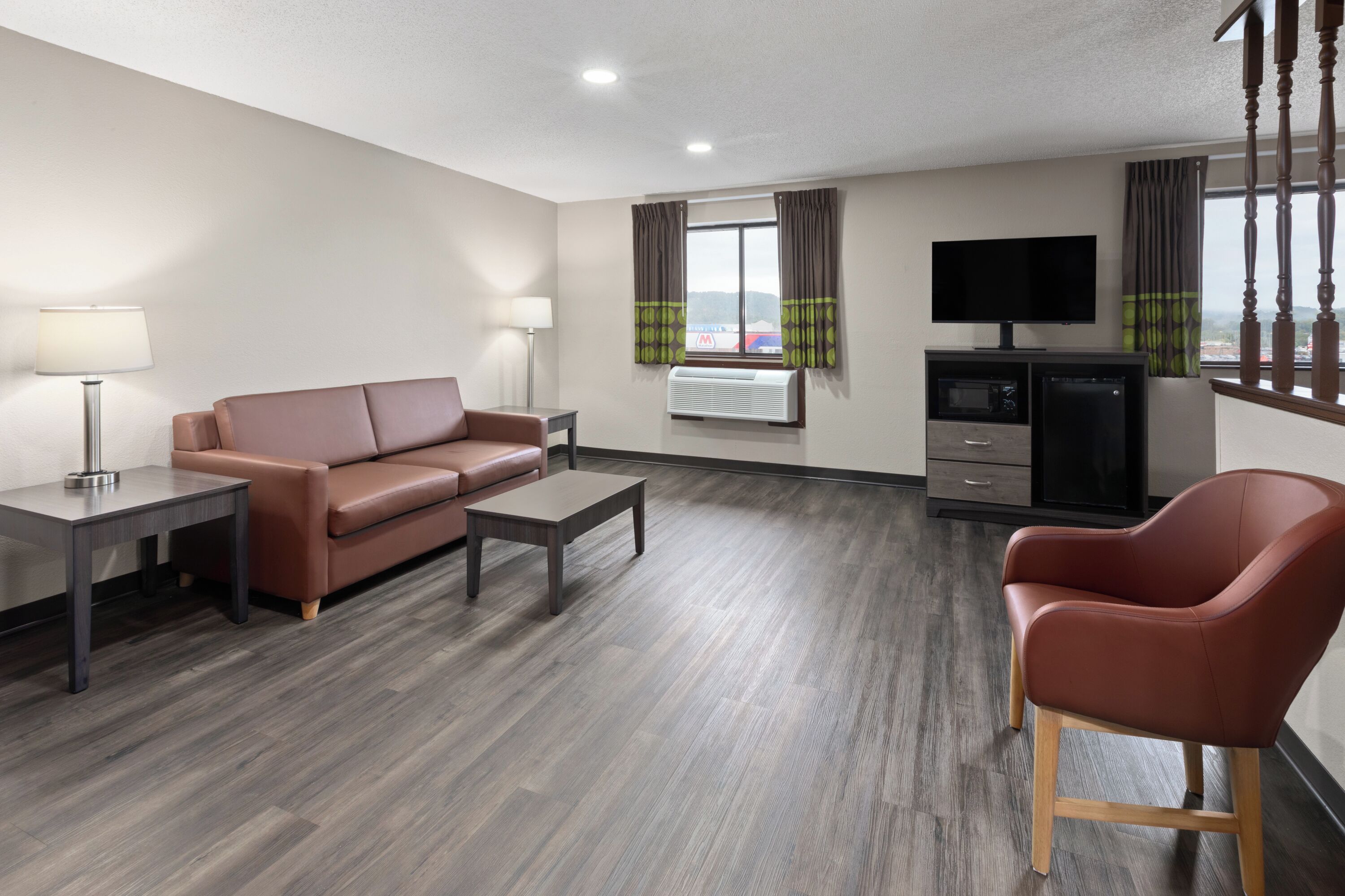 A modern hotel room with a brown leather sofa, a wooden coffee table, a TV, and a mini-fridge.
