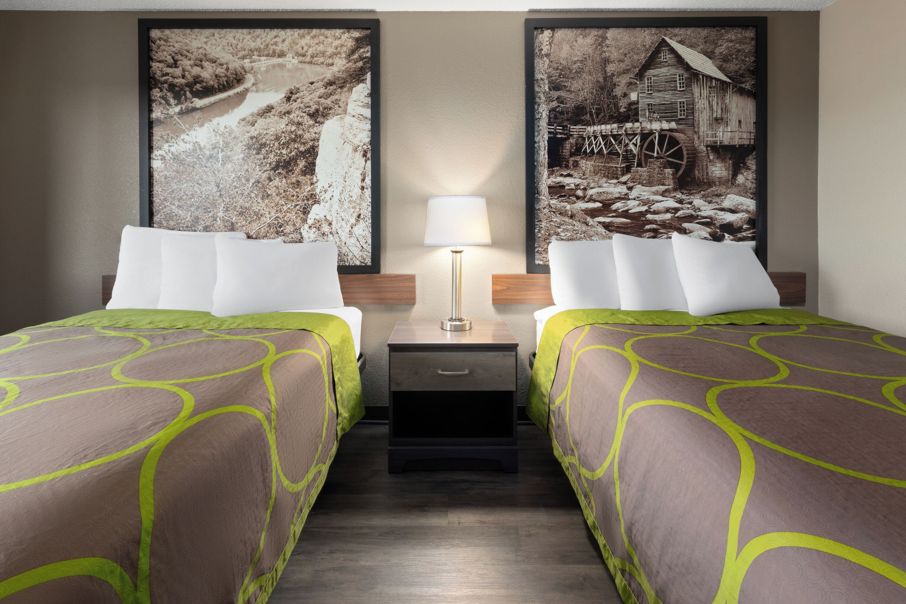 Habitación de hotel con dos camas, una mesita de noche con lámpara y dos cuadros grandes en la pared.