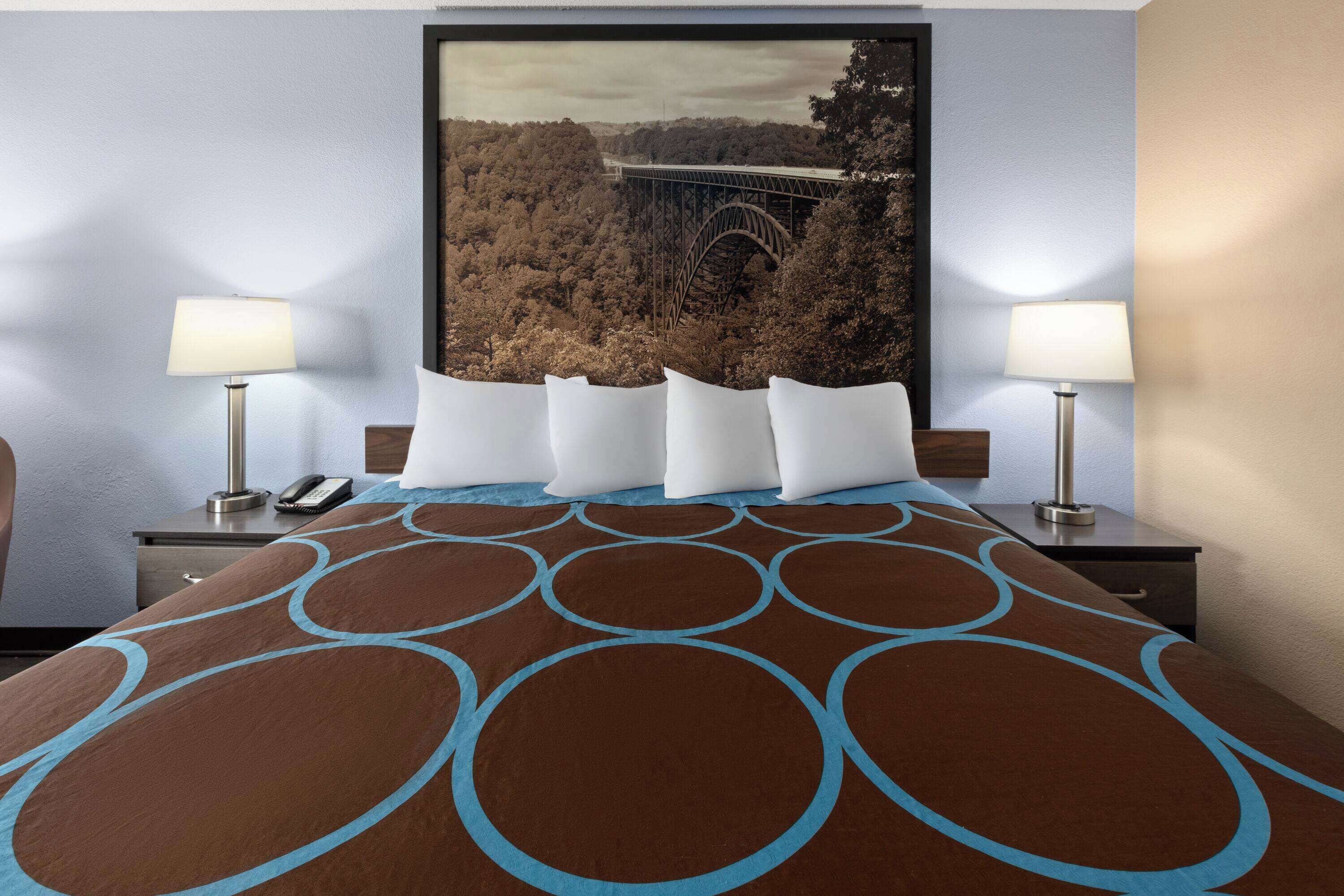 A hotel room with a large bed, two bedside tables, a nightstand, and a framed picture of a bridge.