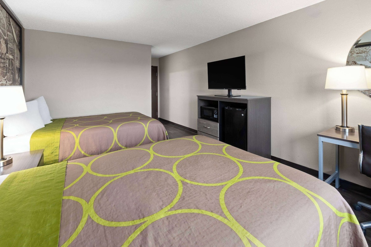 A hotel room with two beds, a television, a desk with a lamp, and a microwave.