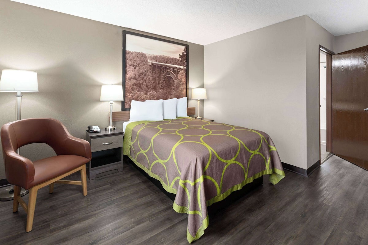 A hotel room with a bed, a chair, a nightstand, and a wall-mounted lamp.