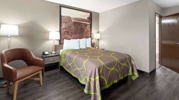A hotel room with a bed, a chair, a nightstand, and a wall-mounted lamp.