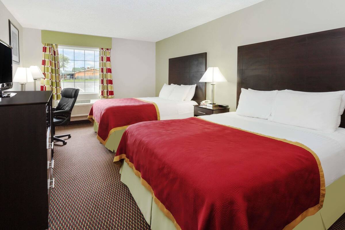 A hotel room with two beds, a desk, a chair, a TV, and a window with curtains.