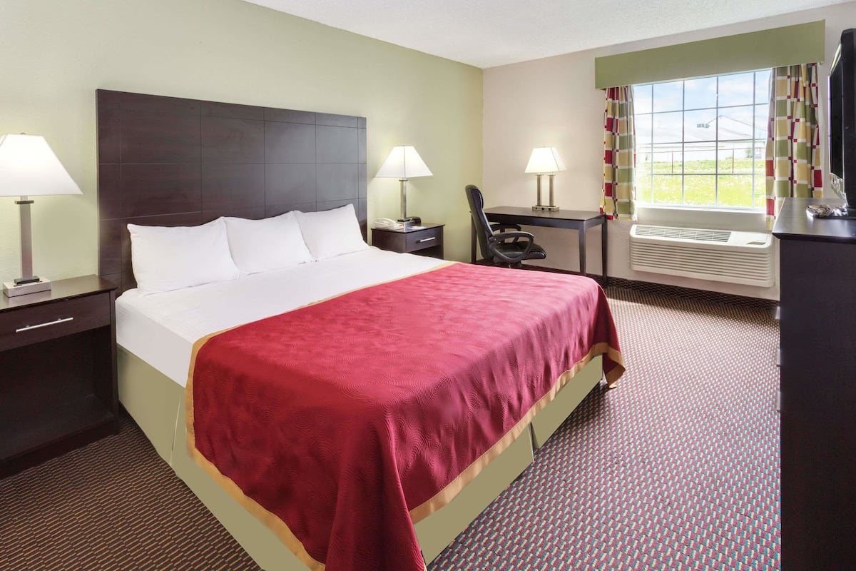 A hotel room with a large bed, two bedside tables with lamps, a desk with a chair, and a window with curtains.