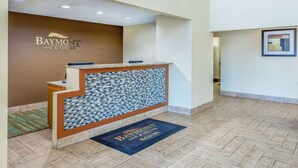 Un área de recepción con el letrero de Baymont Inn & Suites, un muro de mosaicos y piso de madera.