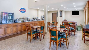 Un rincón de desayuno con mesas y sillas de madera, un refrigerador y una estación de café.
