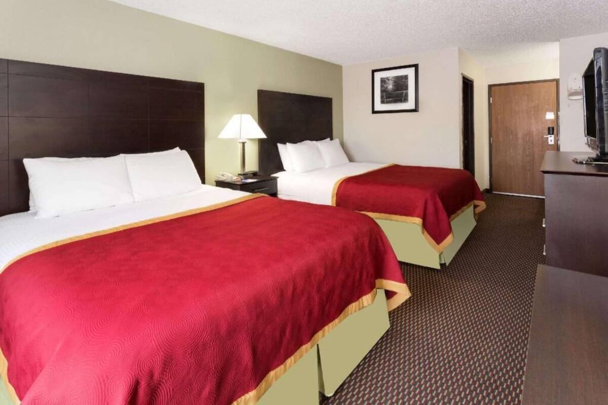 A hotel room with two beds, a desk, a lamp, a TV, and a door.